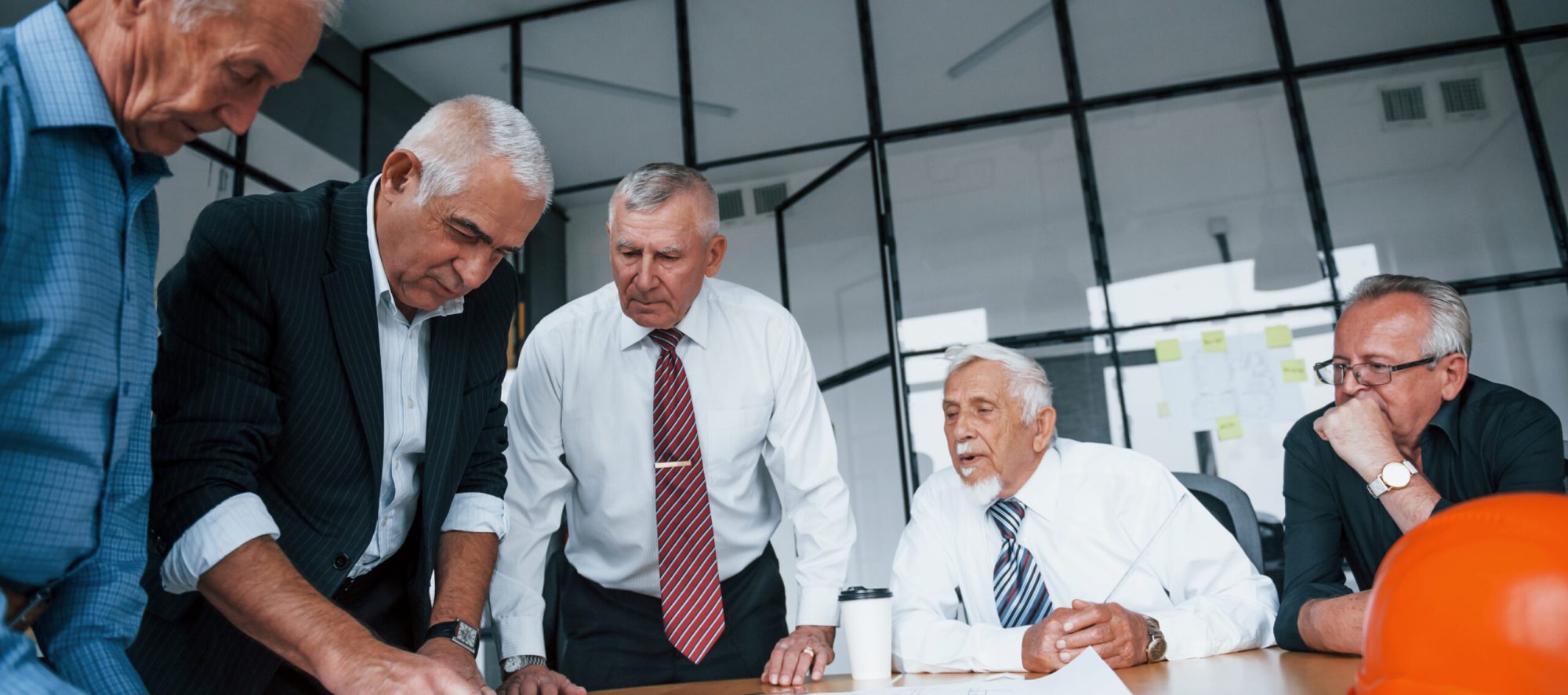 Planning construction by measuring it on paper. Aged team of elderly businessman architects have a meeting in the office.